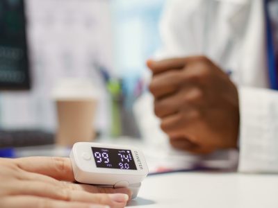 Physician using an oximeter on patient to measure oxygen levels and saturation, checking vital signs during examination at facility. Medic consulting a woman on health insurance. Close up. Camera B.